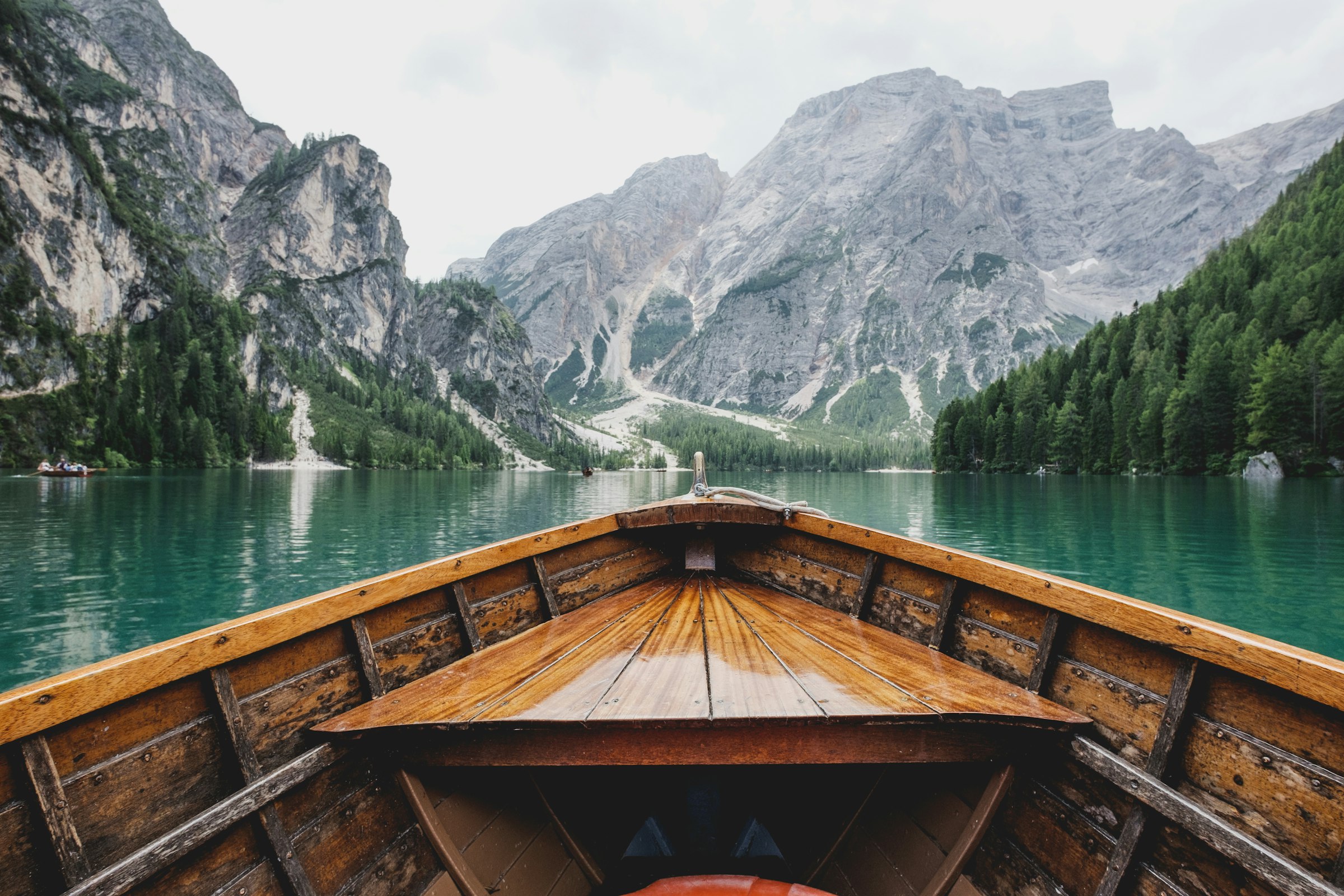 The bow of a wooden boat gliding across a still alpine lake toward the mountains